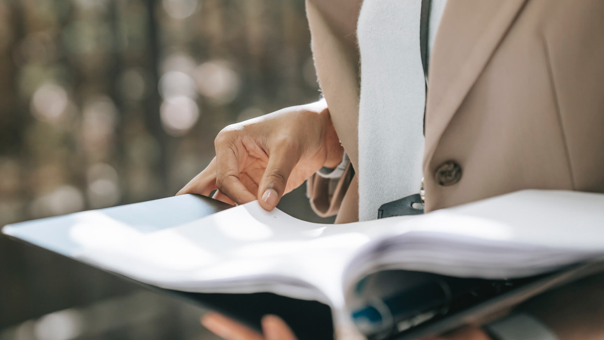 Professional in a beige suit reviews documents in a sleek binder, exuding focus and organization for business settings.