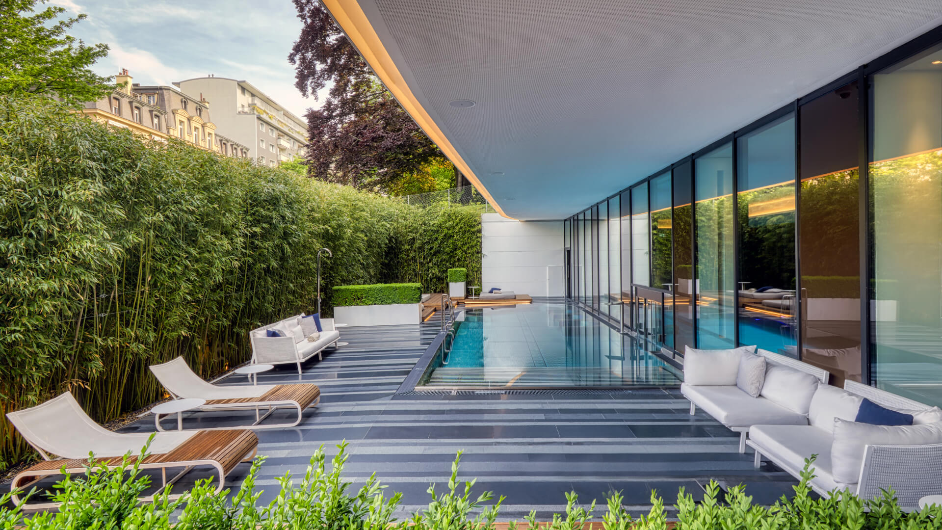 Sleek outdoor pool area with transparent glass walls and lush greenery, creating a serene, luxurious retreat for relaxation.