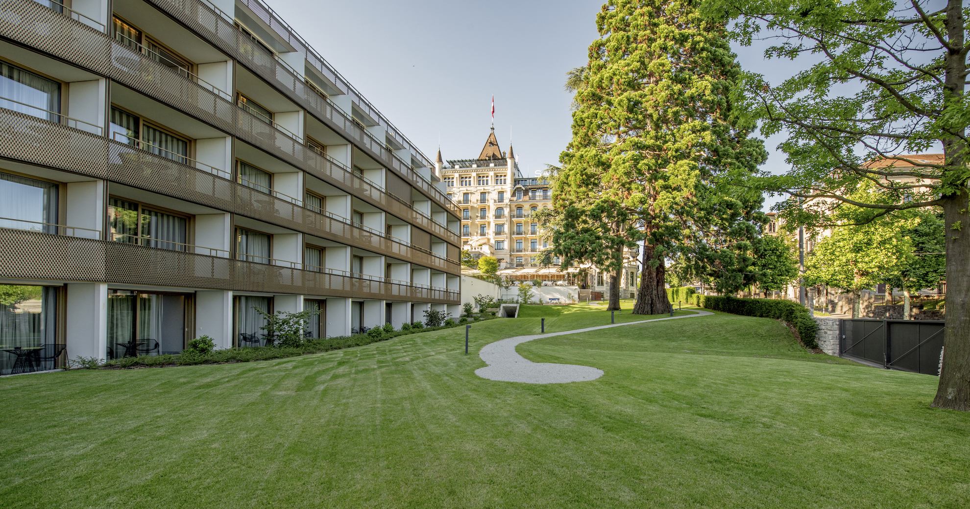 Lush green lawn leading to modern multistory buildings with classic architecture in the background, suggesting serenity in urban living.