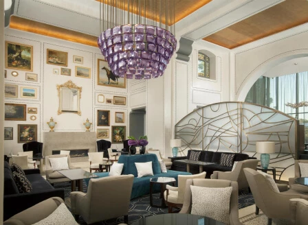 Luxurious hotel lobby with a striking purple chandelier, elegant furnishings, and art-adorned walls, evoking an upscale and welcoming ambiance.
