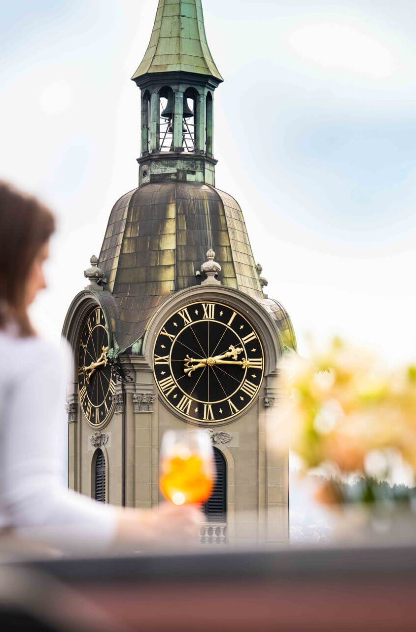Elegant cityscape featuring a woman observing a historic clock tower, capturing a moment of serene reflection in urban life.