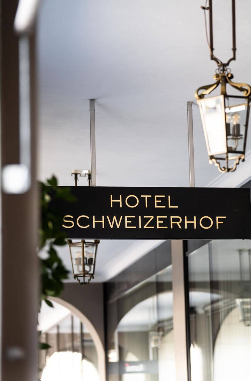 Elegant hotel sign, 'Hotel Schweizerhof', set against a soft, gray entrance, evoking a classic and welcoming ambiance for travelers.