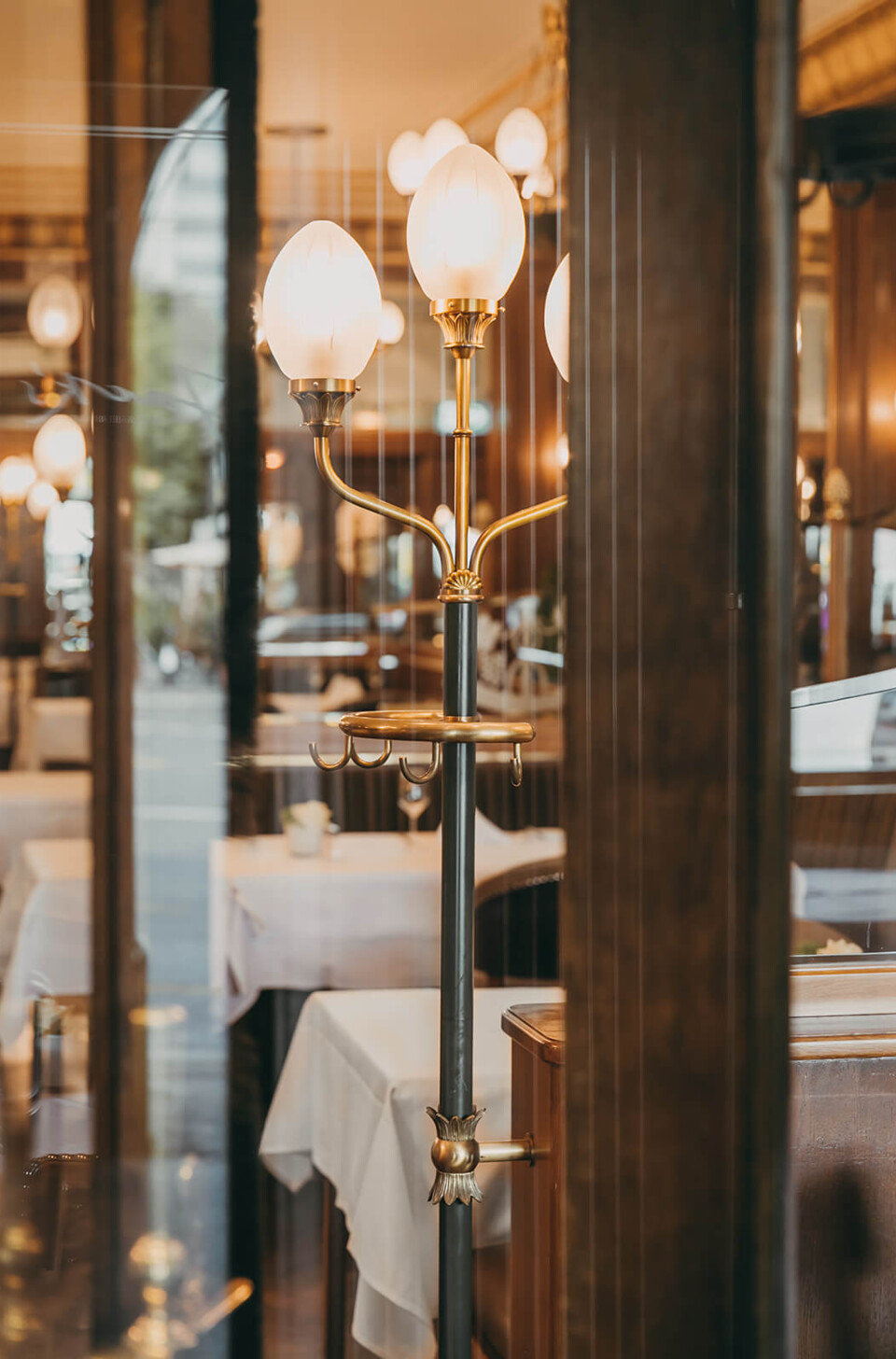 Elegant brass coat stand with glowing white lamps in a sophisticated restaurant setting, evoking warmth and upscale hospitality.