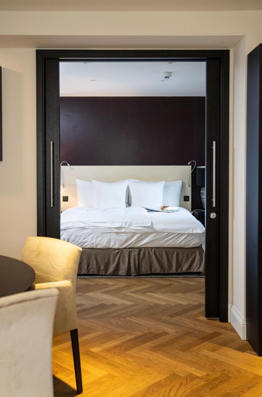 Elegant hotel room with a white bed, dark walls, and wooden floors, creating a cozy and sophisticated atmosphere for travelers.