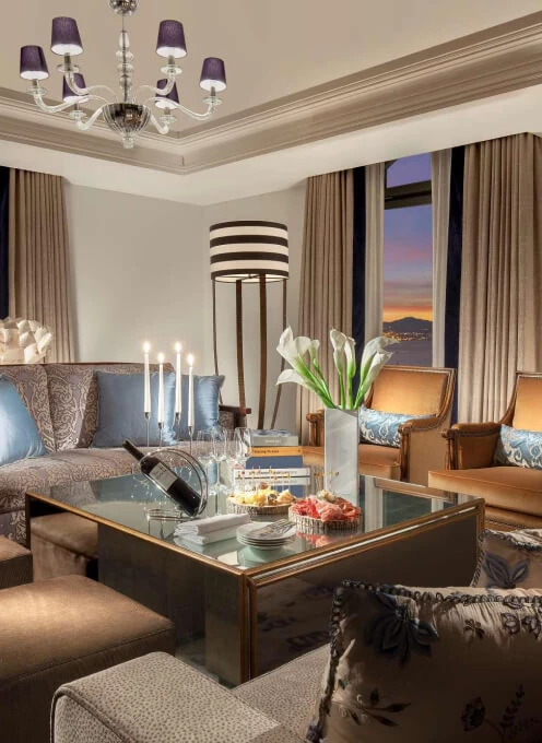 Elegant living room with twilight view through large windows, featuring a chandelier and glass-top table, expressing a serene, upscale retreat.